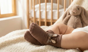 Baby's feet wearing brown socks with a bow, lying on a soft surface in a cozy room.